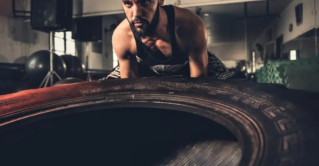 Man focusing intensely while flipping a large tire during a crossfit workout in a gym.